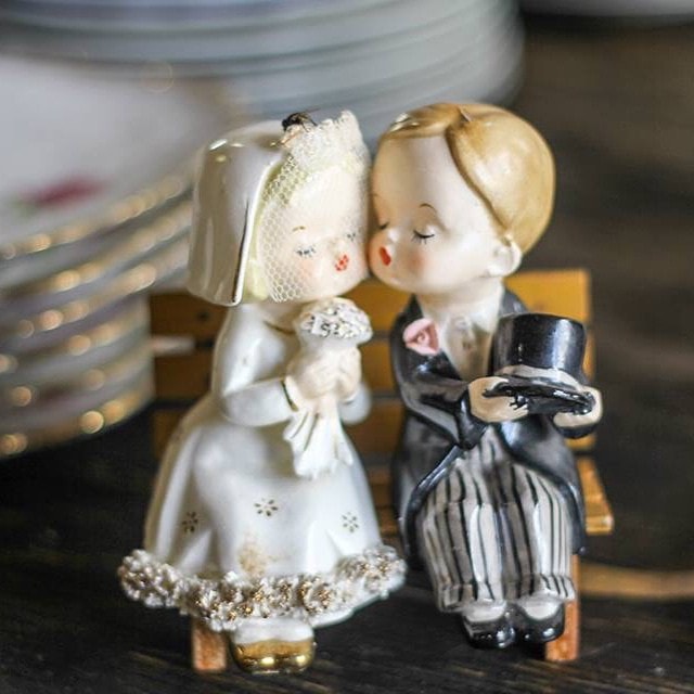 Vintage bride & groom figurines sitting on a bench, kissing - from Lovegood Wedding & Event Rentals collection
